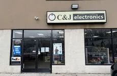 C&J Electronics storefront with glass doors, tan facade, and a FedEx sign on the left