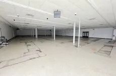Empty unfinished basement with concrete floor, support columns, and exposed ceiling tiles