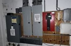 Electrical panels and meter boxes mounted on a wooden basement wall, including a red panel.