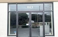 Glass storefront entrance with double doors, address 1023 above, and reflections of trees outside