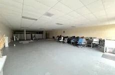 Spacious empty office room with desks, chairs, and fluorescent ceiling lights