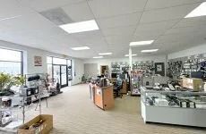 Bright retail showroom with glass display cases, counters, and merchandise under fluorescent lights