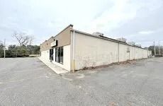 Empty beige commercial building beside a wide asphalt lot under an overcast sky