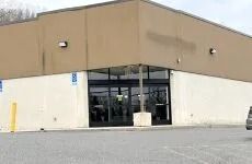 Storefront entrance of a tan building with glass doors and a mostly empty parking lot