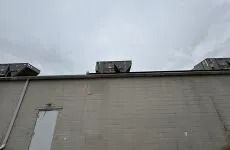 Gray industrial building wall under cloudy sky with rooftop equipment and solar panels