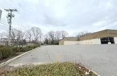 Empty parking lot beside a tan industrial building under a cloudy sky