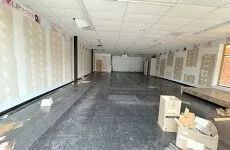 Empty commercial room with black floor, white ceiling tiles, and boxes stacked near the right wall
