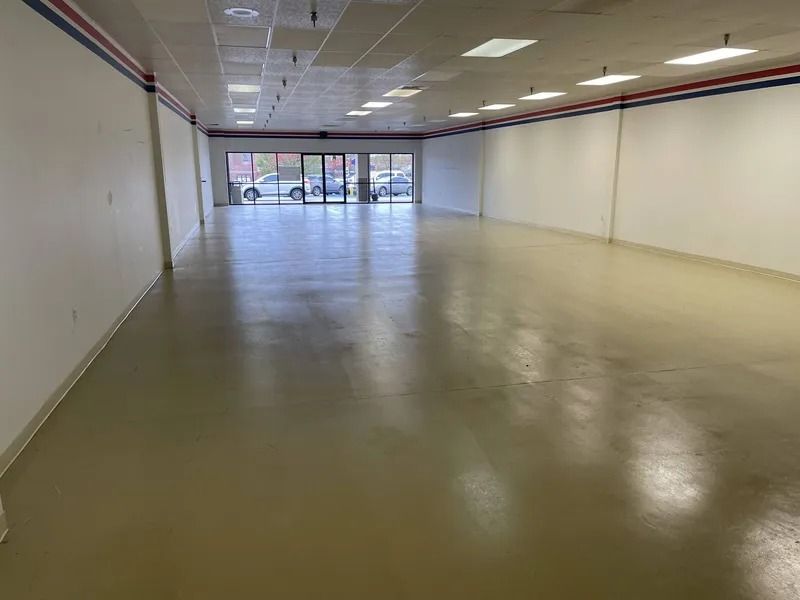 Empty indoor storefront with beige floor, white walls, and glass entrance doors at the far end