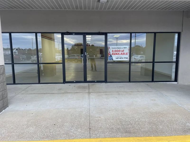Glass storefront with a “For Lease” sign under an overhang on a concrete walkway.