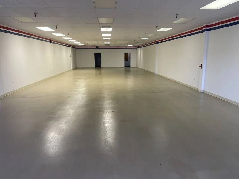Empty fluorescent-lit warehouse room with polished concrete floor and white walls