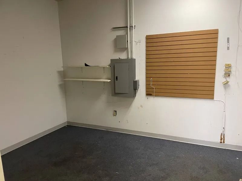 Empty room with white walls, dark carpet, and mounted shelves and cabinet.