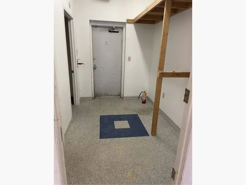 Narrow utility room with gray floor, white walls, a closed door, and a blue mat in the center.