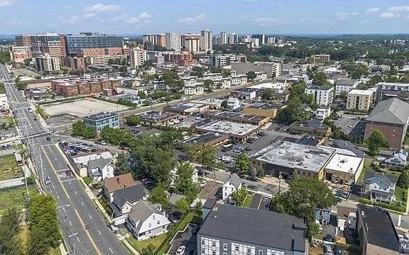 Aerial view of a city neighborhood with streets, houses, shops, and mid-rise buildings under a clear sky