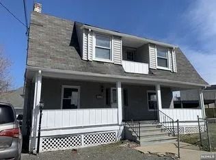 Two-story white house with gray roof, front porch, and black shutters on a sunny day