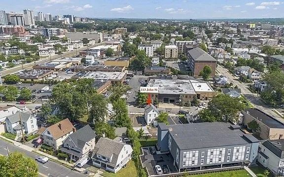 Aerial view of a suburban neighborhood with houses, trees, and mid-rise buildings under a bright sky