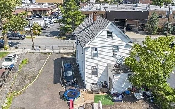 Aerial view of a gray house beside a parking lot, with a tree and nearby buildings.