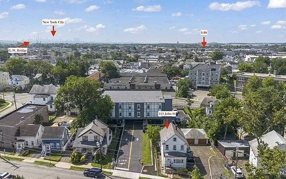 Aerial view of a residential neighborhood with houses, trees, and distant city skyline under a blue sky.