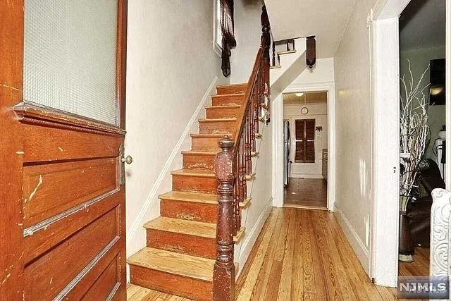 Interior hallway with wooden staircase, hardwood floors, and white walls
