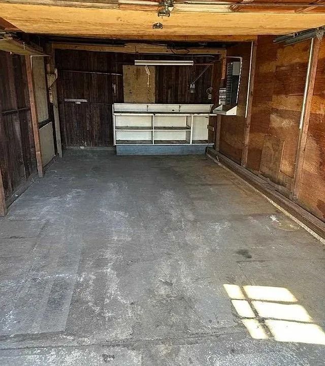 Empty wooden garage interior with concrete floor and a small workbench at the back.