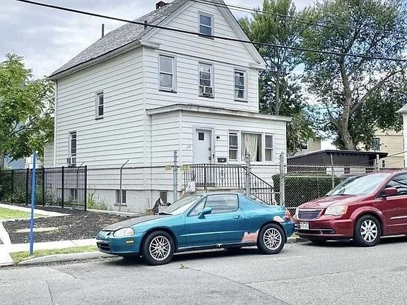Two parked cars beside a white house with a fenced yard on a residential street.