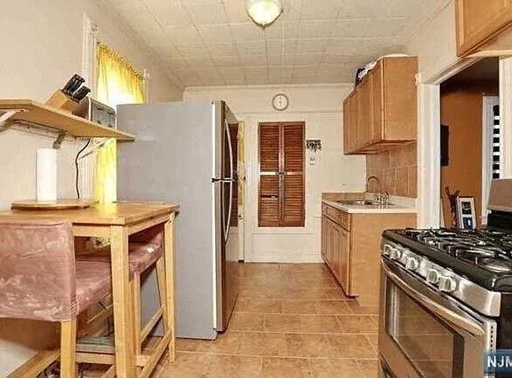 Narrow kitchen with tan tile floor, white refrigerator, wooden cabinets, and a gas stove.