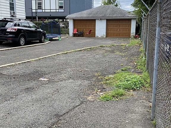 Gravel driveway beside chain-link fence and garage, with parked black car and small red chair.