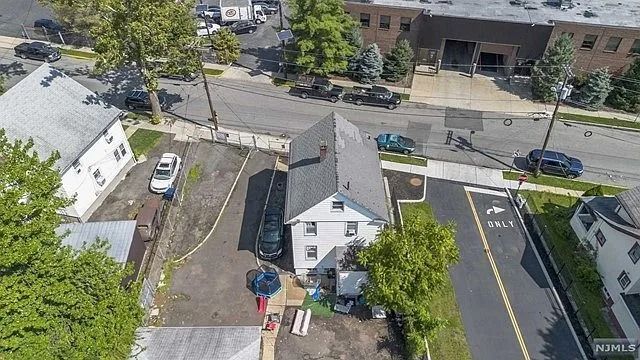Aerial view of a small white house, parked cars, and a street with a large apartment building nearby.