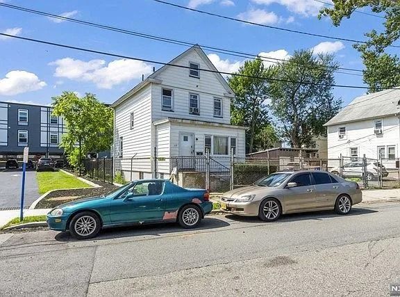 Two parked cars in front of a white house on a sunny residential street