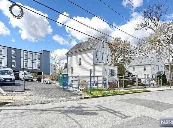 Small white house beside an apartment building under a blue sky with power lines and parked cars