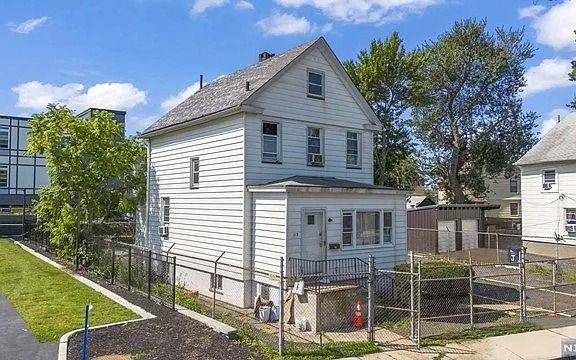White two-story house with a small porch and fenced yard on a sunny residential street.