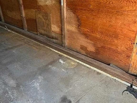 Empty garage floor beside a wooden wall with a small crack near the baseboard