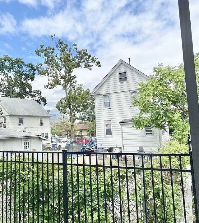White houses behind a black railing, with trees and a cloudy sky in a residential area.