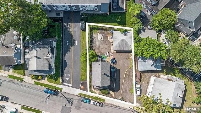 Aerial view of a residential property with a house, driveway, yard, and neighboring homes along a street.