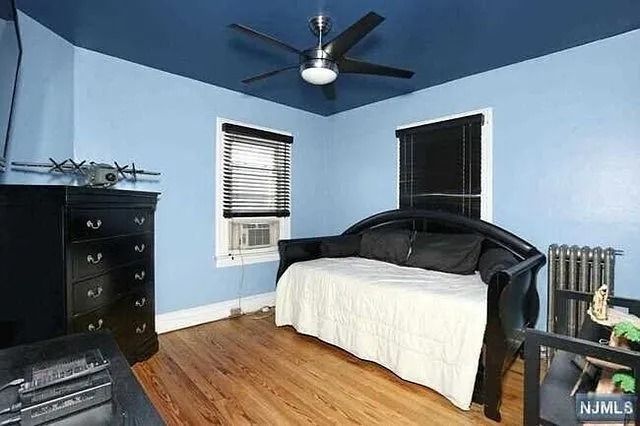 Blue bedroom with black bed, dresser, windows, ceiling fan, and hardwood floor