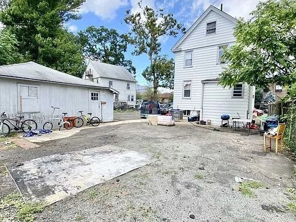 Gravel backyard with a white house, garage, scattered bicycles, and a concrete slab under a blue sky