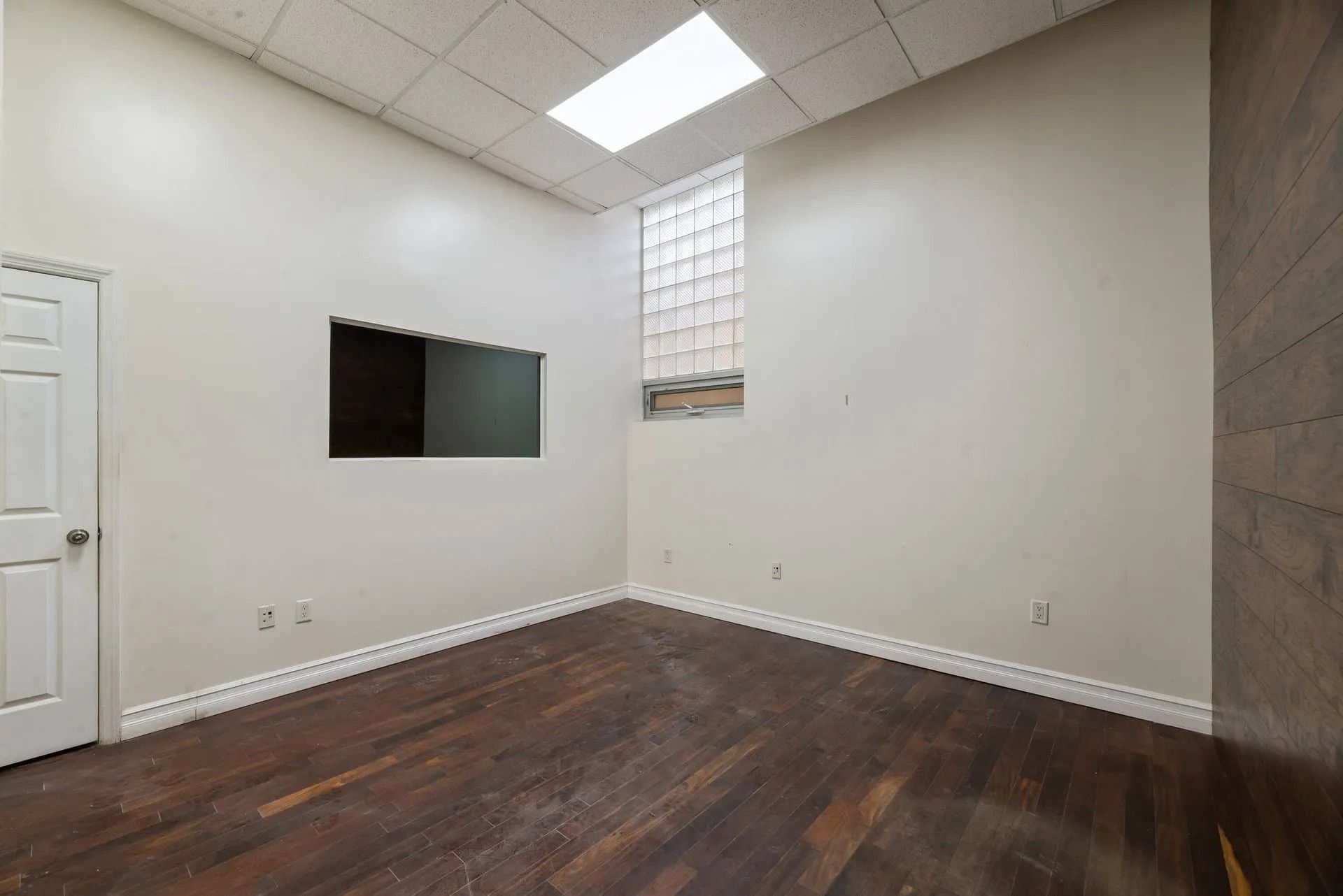 Empty room with dark wood floor, white walls, skylight, and a small wall-mounted mirror.