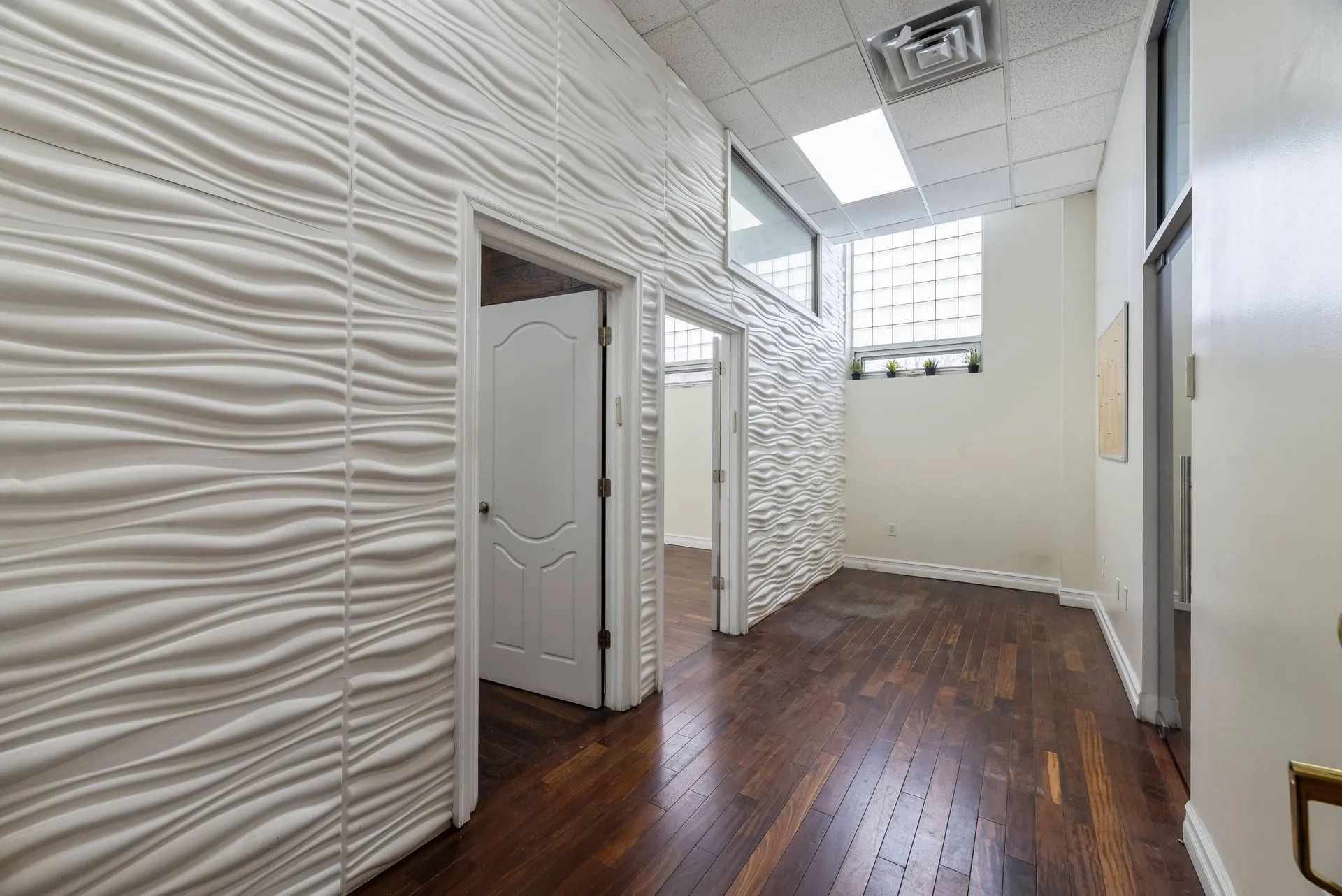 Bright hallway with textured white walls, dark wood floor, and tall windows near the end.