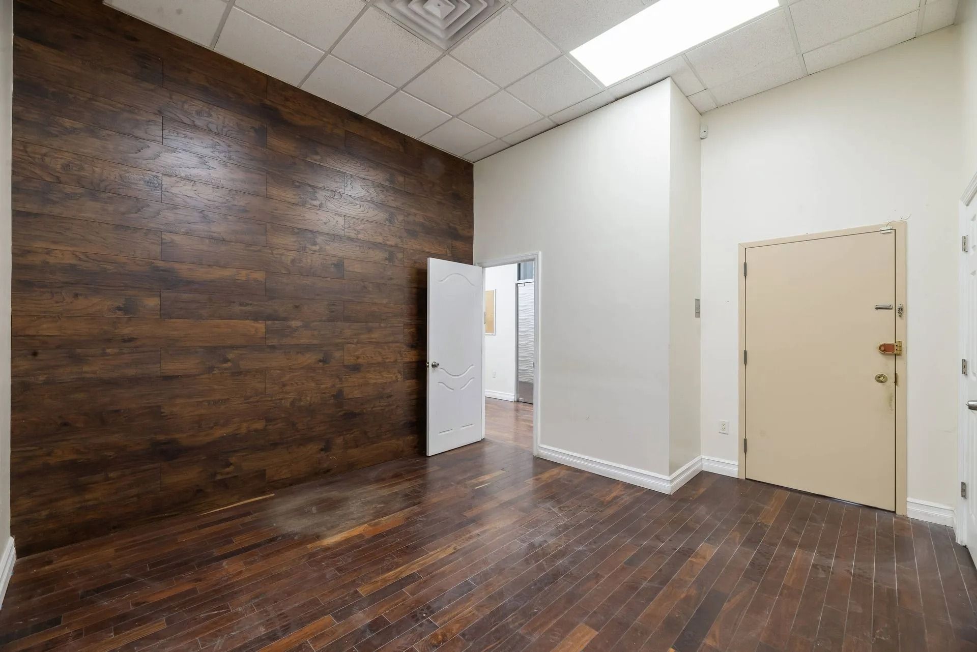 Empty room with dark wood floor, wood accent wall, white walls, and open doorways