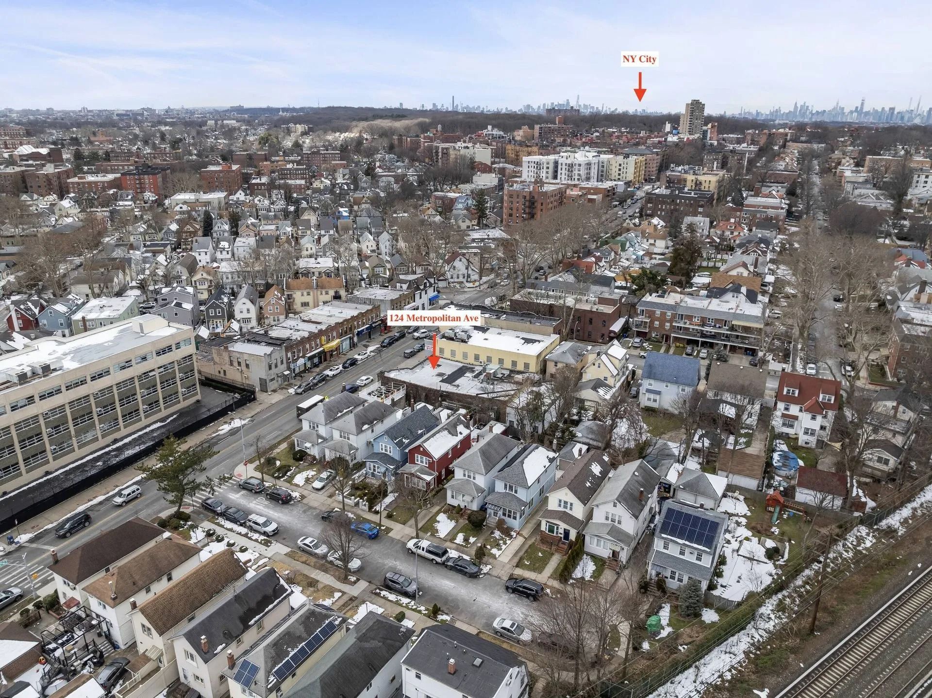 Aerial view of a snowy residential neighborhood with houses, streets, and a large building in the foreground.
