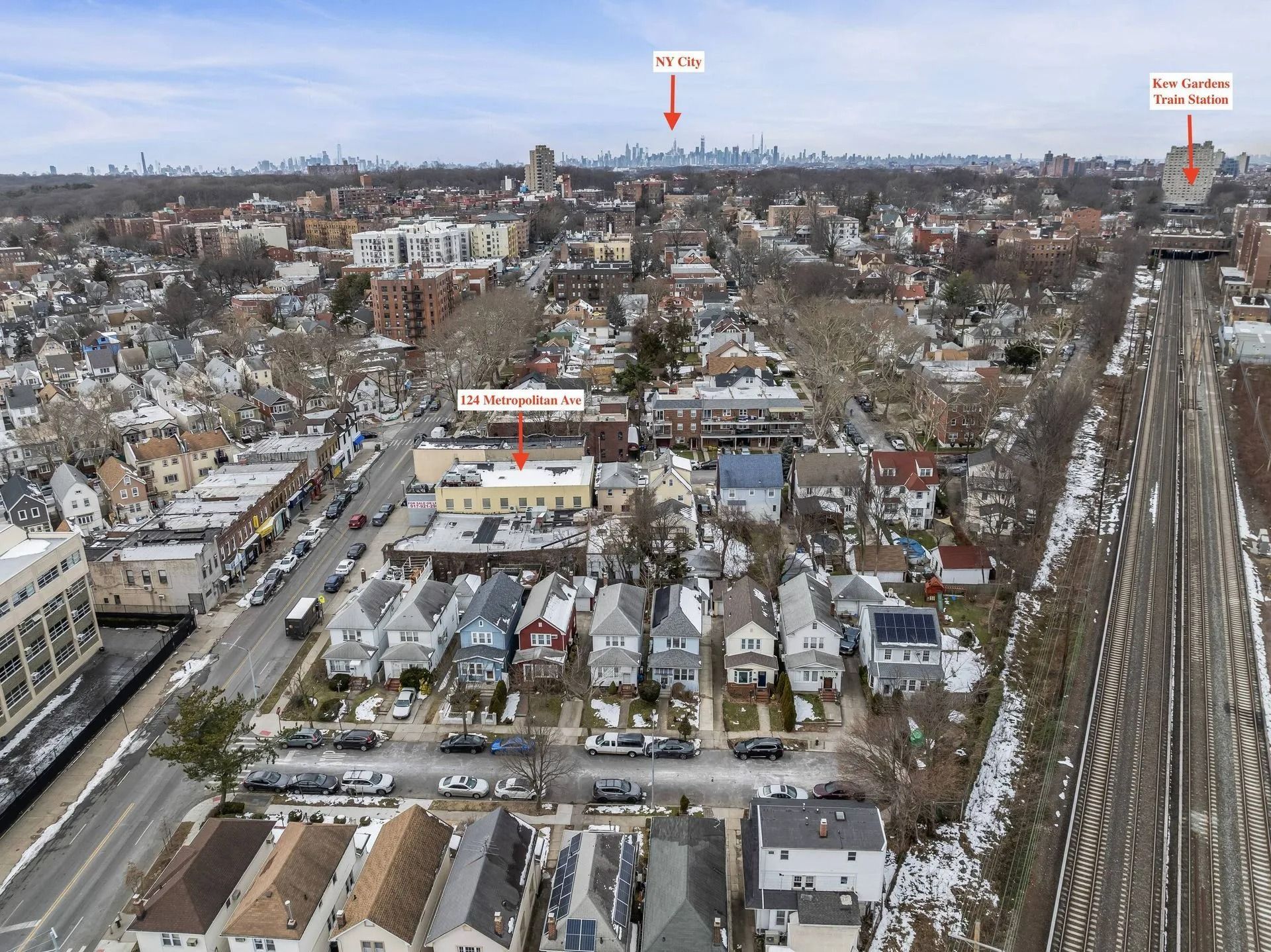 Aerial winter view of a snowy suburban neighborhood with houses, roads, and a railway line.