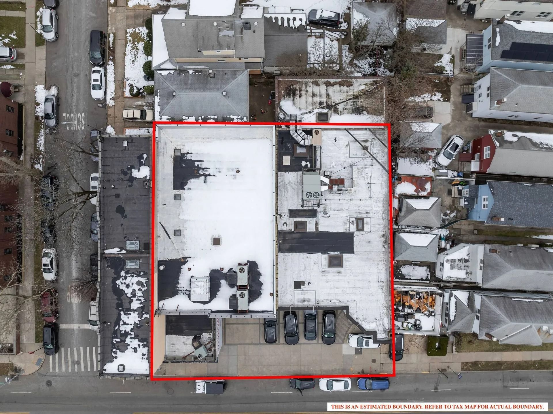 Aerial view of a snow-covered building and parking lot outlined in red on a city street.