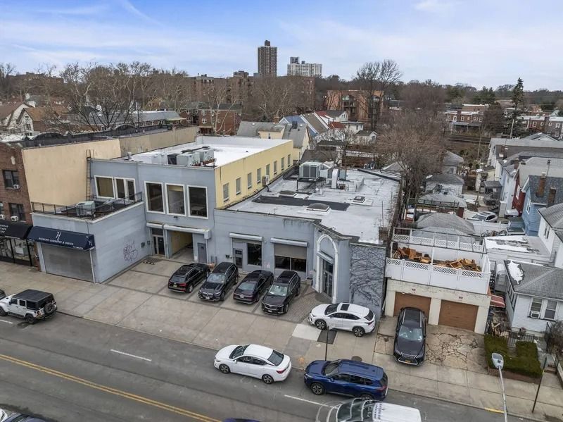 Street view of low-rise buildings, parked cars, and leafless trees under an overcast sky.