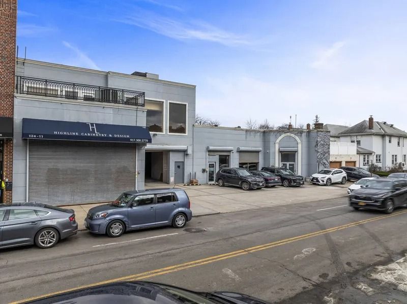 Street view of a gray storefront and white buildings with parked cars along the road