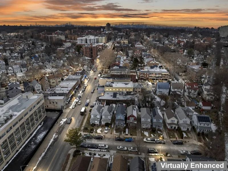Aerial view of a snowy suburban neighborhood at sunset with cars on a lit main road.