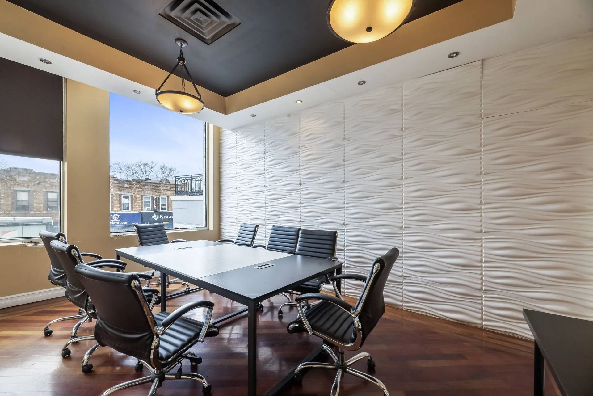 Conference room with table, rolling chairs, and textured white wall under warm ceiling lights