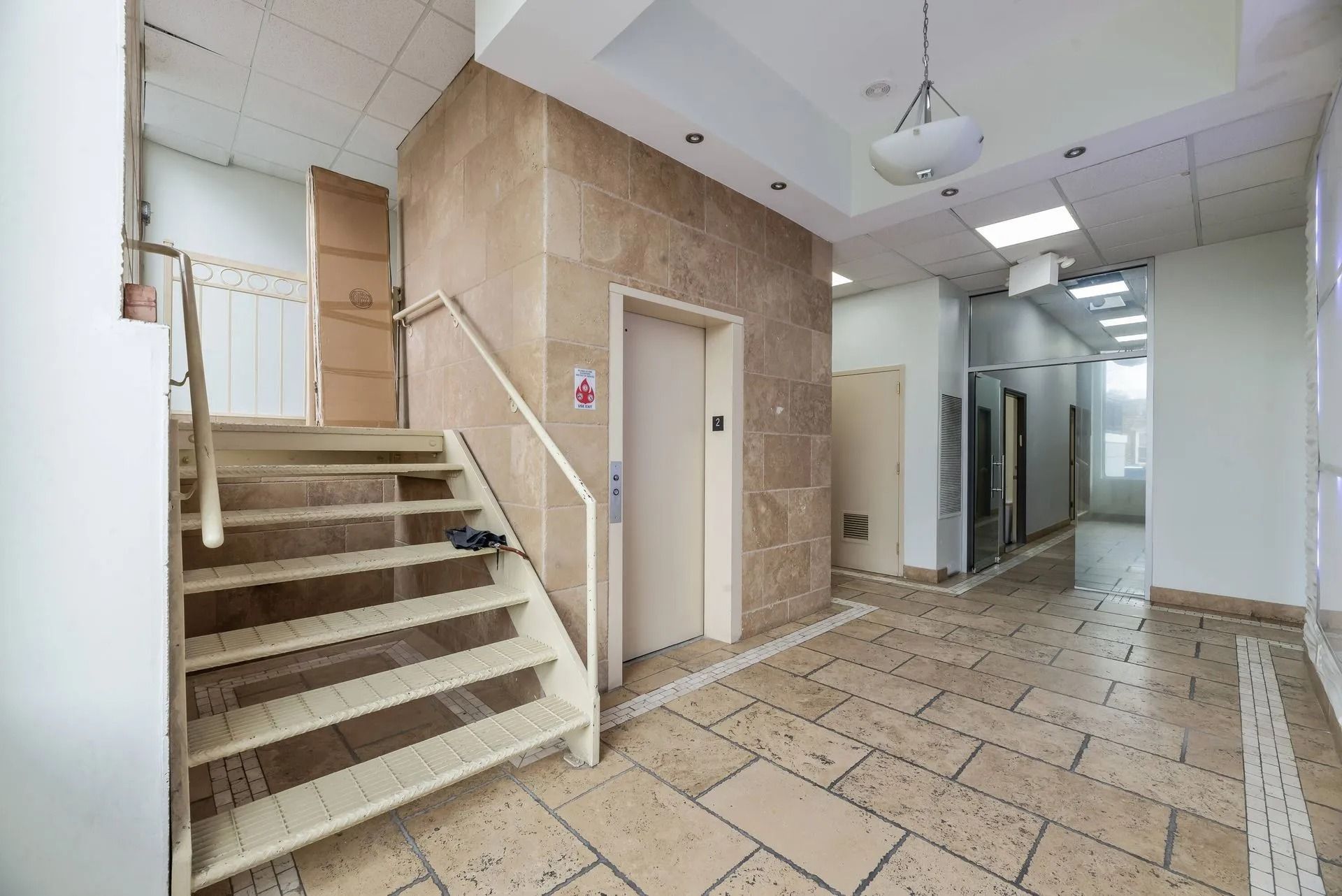 Interior hallway with stairs, elevator door, and tiled floor in a building lobby