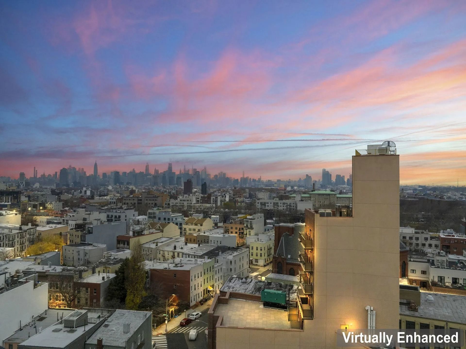 City skyline at sunset with pink clouds over low rooftops and a tall beige building in the foreground
