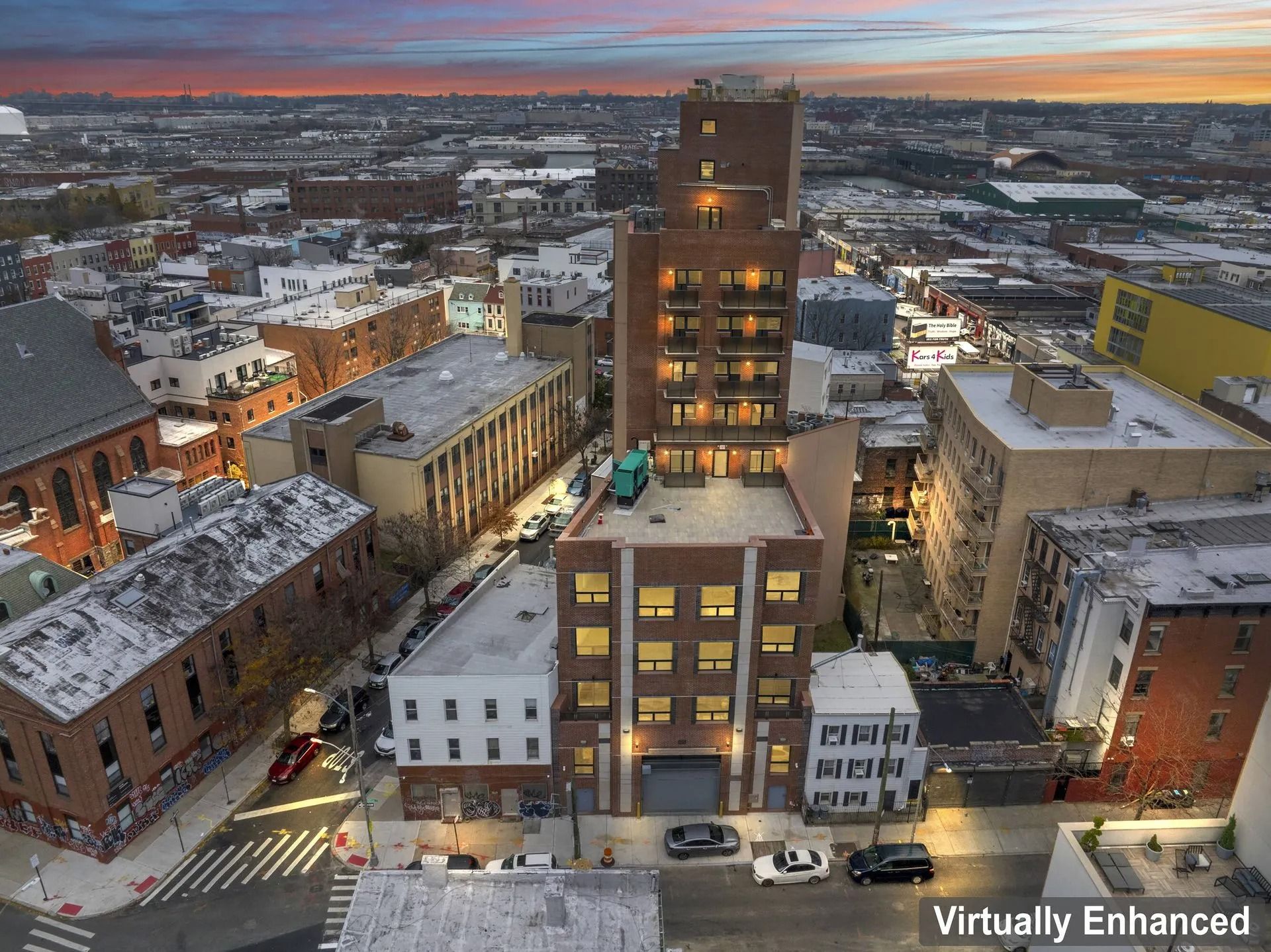 Snowy downtown cityscape at sunset with a tall lit building centered among lower brick buildings.