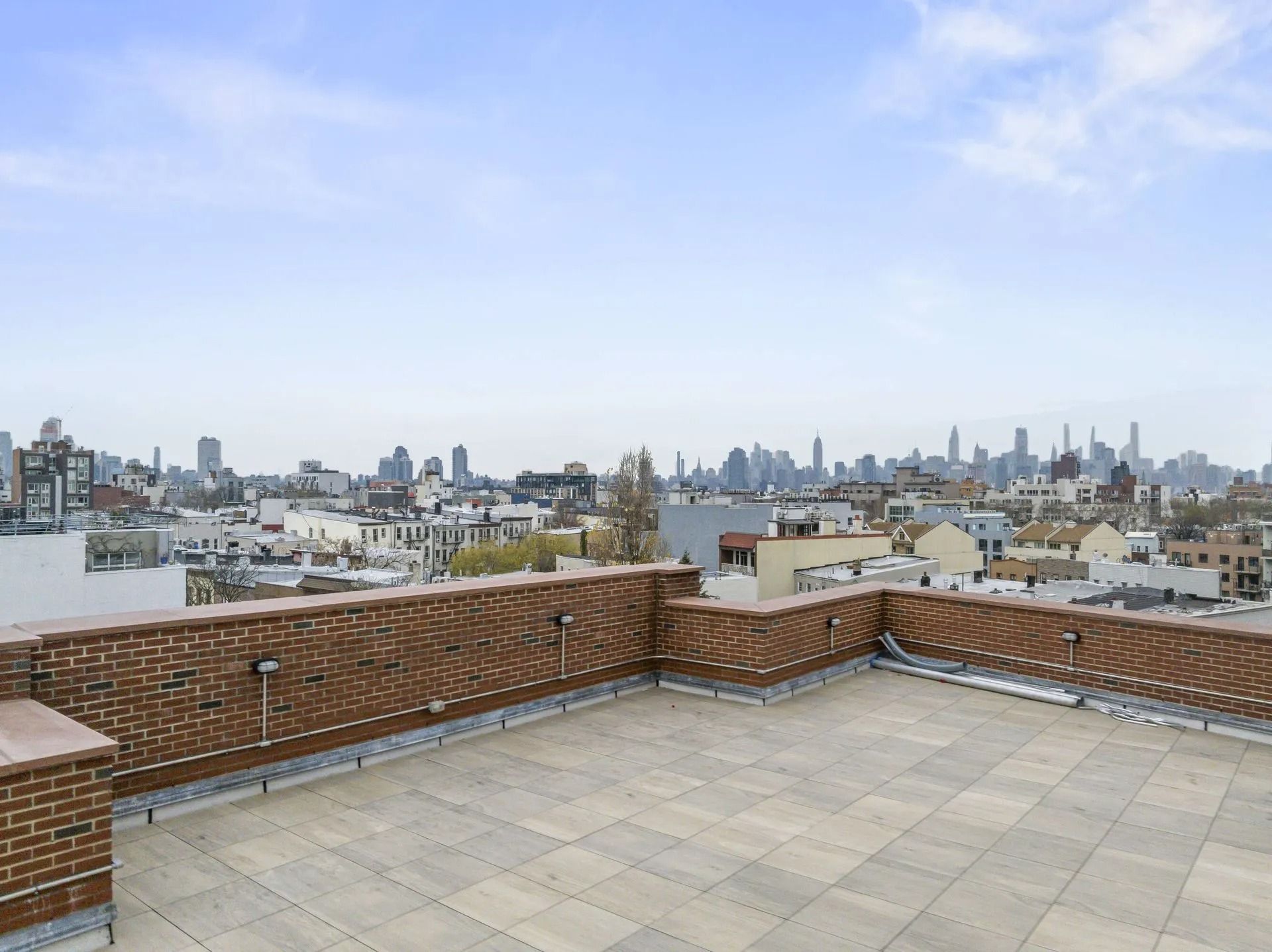 Rooftop terrace with brick walls overlooking a city skyline under a clear blue sky.
