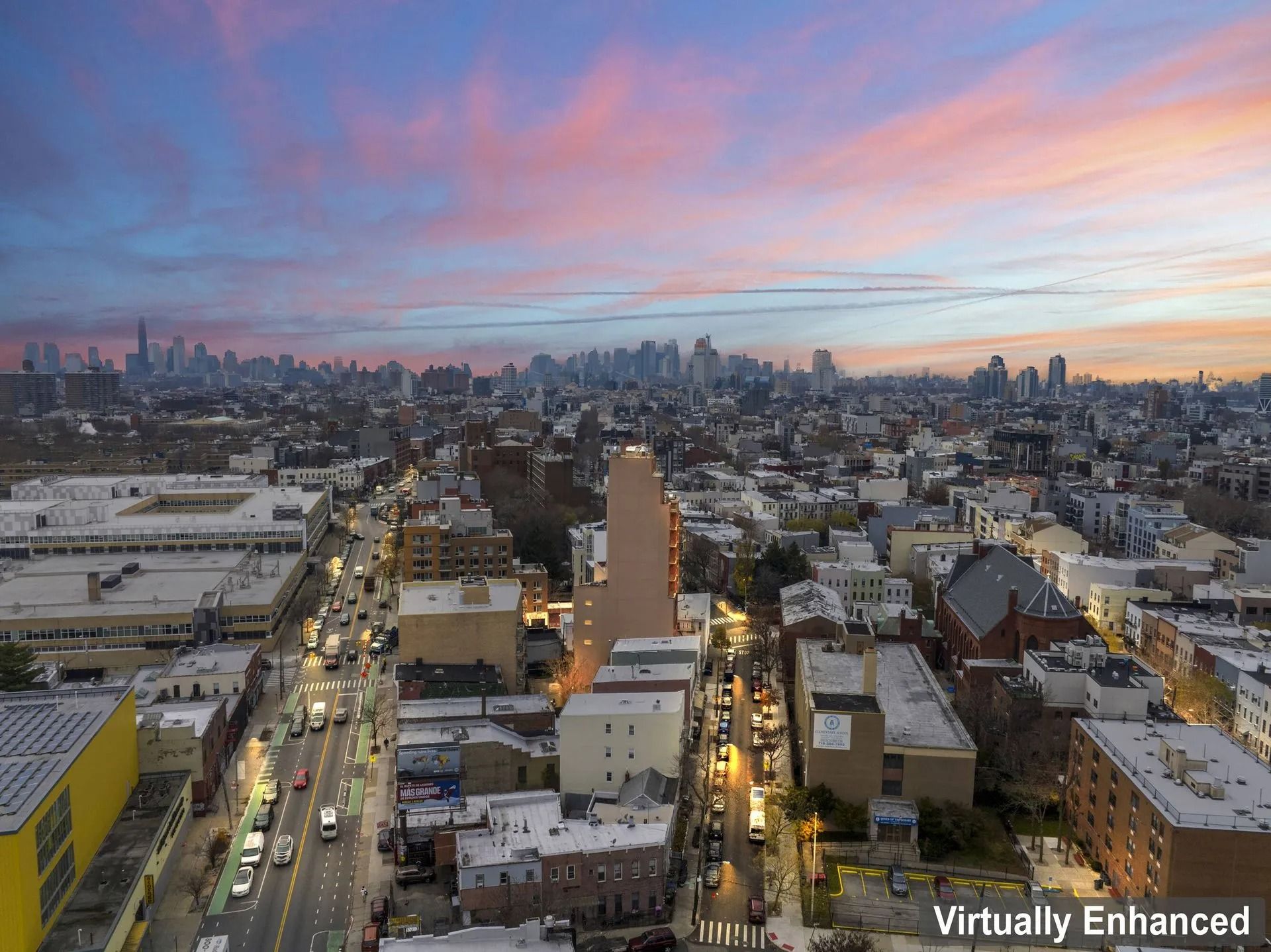 City skyline at sunset with pink clouds above a dense urban neighborhood